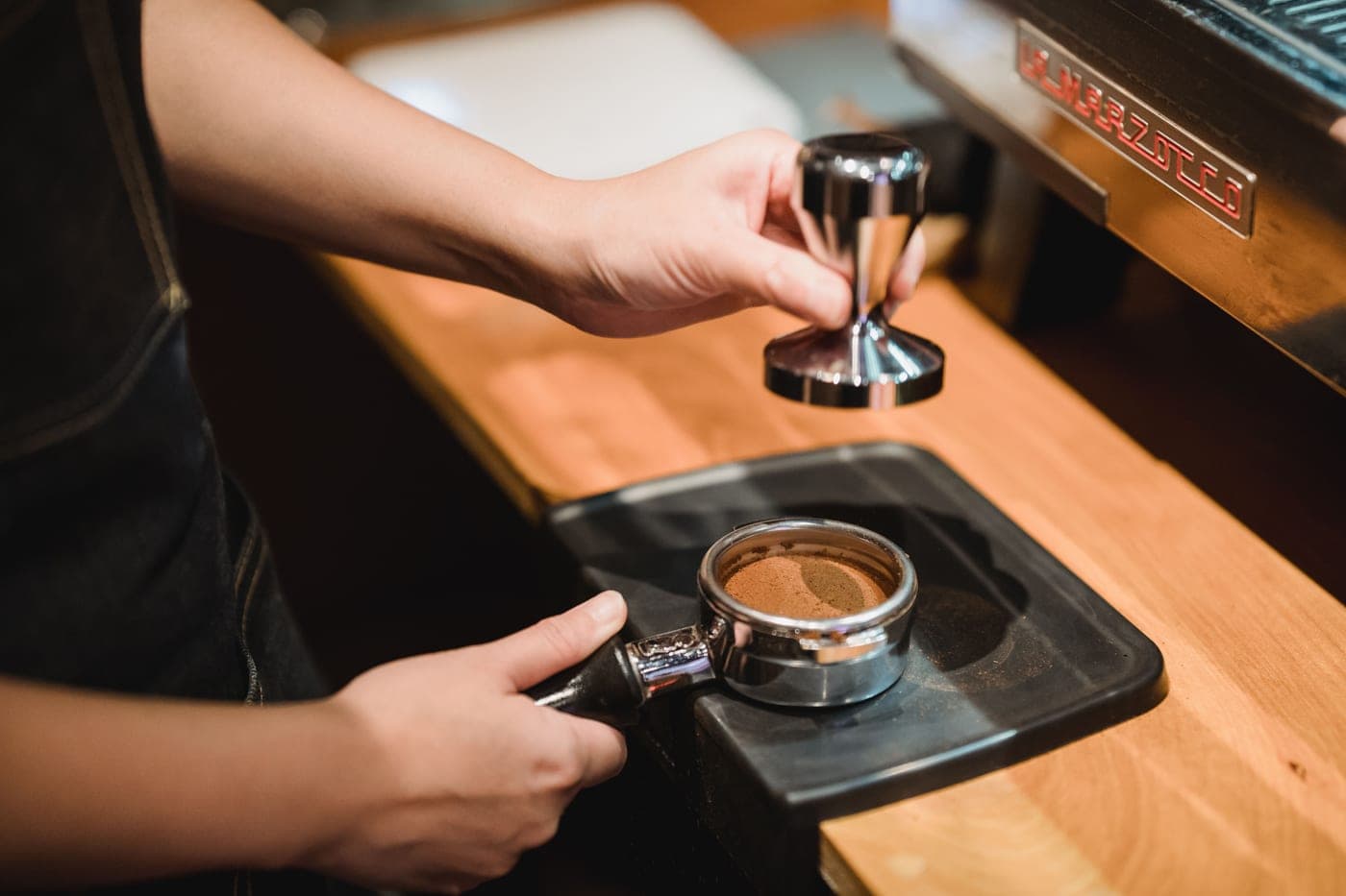 A tamper compressing coffee in a basket